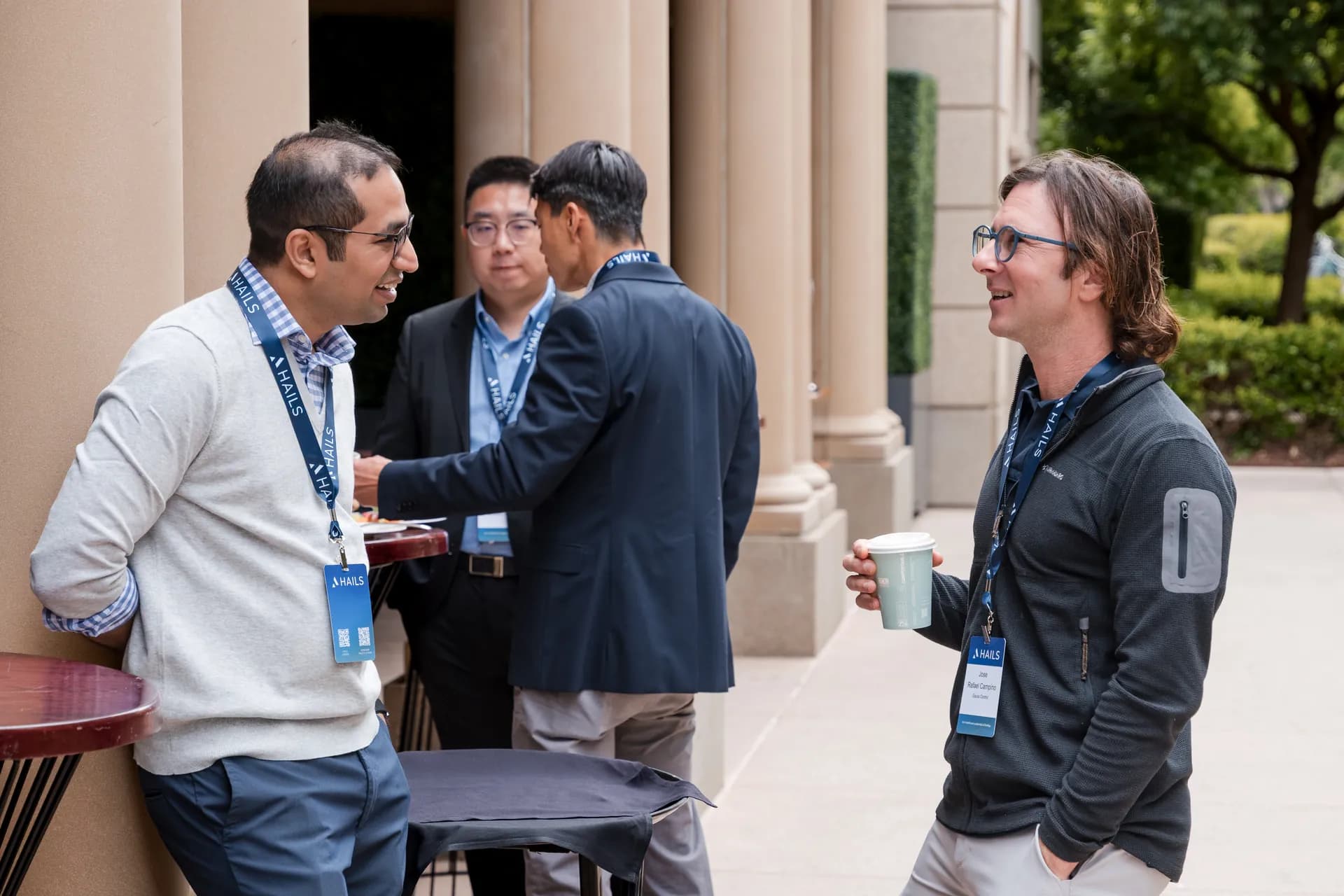 Four attendees talking over coffee on the colonnade outside the hall