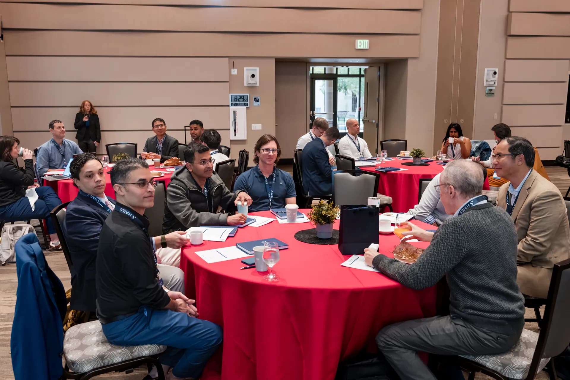 Attendees seated at round red-clothed tables in the hall before a session begins