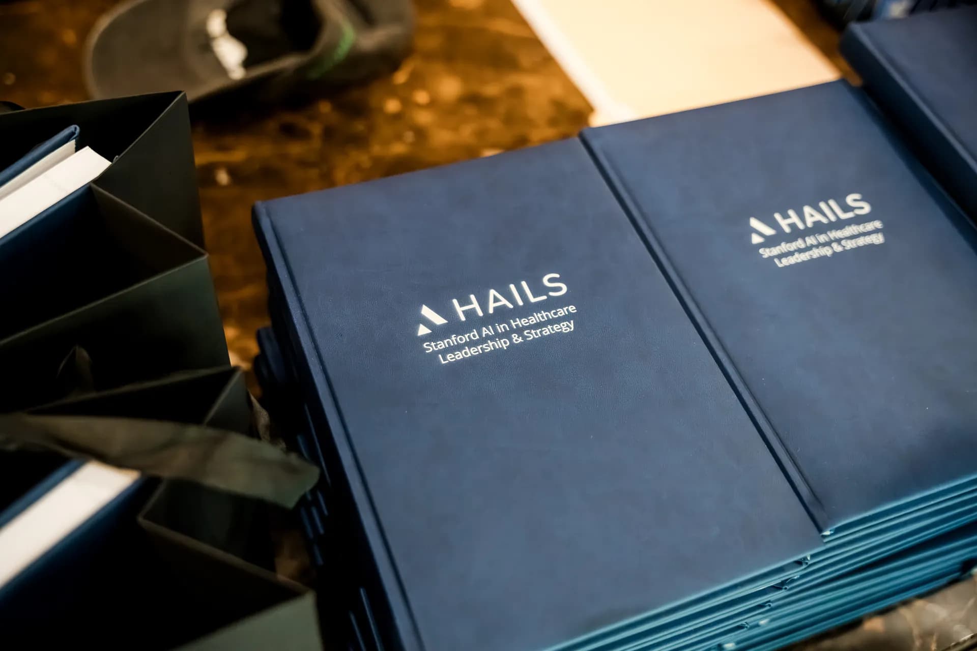 A stack of navy HAILS notebooks reading 'Stanford AI in Healthcare Leadership & Strategy'