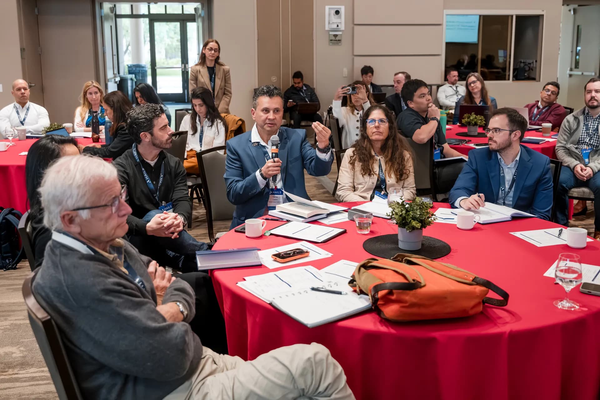 An attendee speaking into a microphone at their table while the room listens